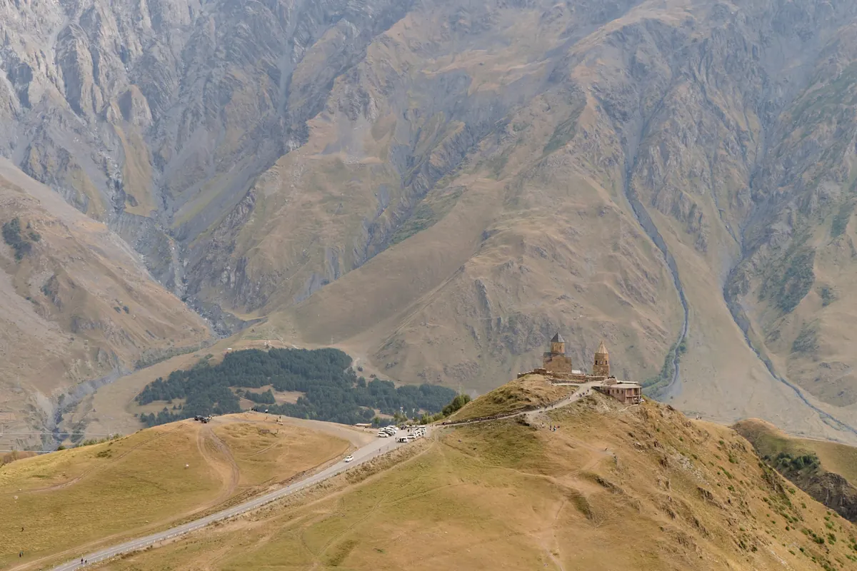 A small stone church on a ridge above a wide valley under bare brown mountains of the Caucasus